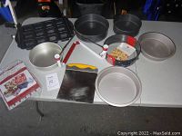Top-down view of various baking pans including round cake pans, rectangular mini loaf molds, and a springform pan with latch on white table.