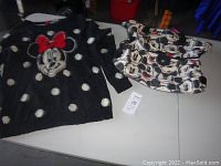 Photo of black fuzzy knit sweater with white polka dots and Minnie Mouse face with red bow next to a soft fabric purse with multiple Mickey Mouse faces printed.