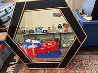 Front view of the hexagon mirror showing the black and gold frame and reflective glass surface.