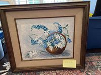Front view of framed floral painting with basket of blue and white flowers, signature visible.