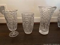 Three European crystal vases grouped on floor showing detailed cut patterns, various shapes and sizes.