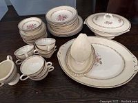 Full set view showing plates, cups, saucers, serving platter, covered vegetable dish, gravy boat and bowls in white eggshell porcelain with floral pattern and gold trim