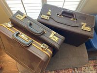 Top view of five briefcases arranged showing leather straps, metal locks and handles on a chair and carpet.