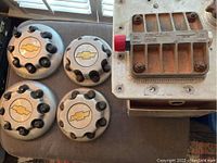Four Chevrolet hubcaps and Racor fuel engine compartment component arranged on surface