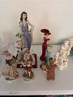 Seven various figurines on display, visible damage to one larger hand-painted Lefton China piece.