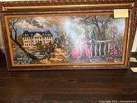 Full view of large framed crochet knit painting showing two figures in historic clothing in outdoor garden scene with building and swans in background.