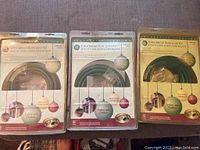 Three boxed Holiday Christmas Super Bright Rope Light Kits with green cords and 18 bulbs each, displayed side by side showing front packaging with ornament graphics and product information.