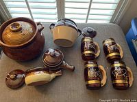 Overview of all items on table showing large jug, smaller pots, lidded handled pots, and four beer mugs.