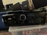 Front angled view of Panasonic SA-HE100 AV receiver with front panel controls and two Bose speakers placed on top with cords wrapped around them.