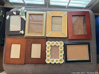 Eight assorted picture frames arranged in two rows on a soft surface under window light