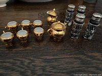 Full view of the lot showing all silver plated salt and pepper shakers and miniature gold plated tea set pieces.
