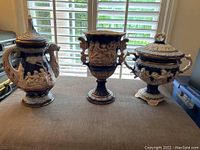Photo of all three vases together on a table, showing their relative size, shape, and decorative relief work