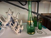 Green liquor decanter and shot glasses alongside white and blue ceramic tea set with floral design