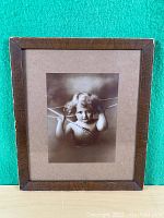 Full view of framed sepia-tone print showing cupid child figure and wood frame