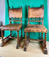 Pair of antique wooden chairs with leather seats and backs, showing detailed wood carving and patina wear