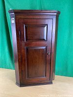 Front view of the antique hanging corner cupboard, showing the single door with two paneled sections and keyhole.
