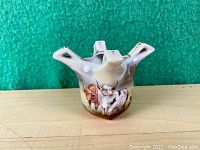 Front view of the porcelain vase showing the painted cattle (brown and white cows) on the body and the four spouted protrusions at the top rim.