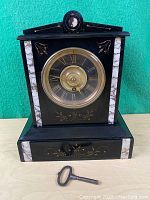 Front view of the black slate mantel clock showing brass bezel and Roman numeral dial with winding key in front