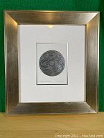 Full image of the framed print in silver-tone frame with white mat and round black and white Haida wolf design.