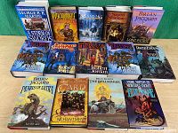 Photo showing all 14 hardcover science fiction and fantasy novels arranged in two rows on a wooden table with green background.