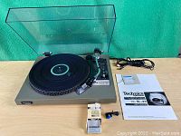 Technics SL-23 turntable with open clear acrylic dust cover, platter, tonearm, RCA cable, instruction manual and cartridge