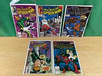 Five issues of The Spectacular Spider-Man comics displayed standing in protective plastic sleeves on a wooden surface with a green backdrop.
