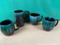 Four Blue Mountain Pottery mugs, one with a star and 'Blue Mountain Pottery' design, showing textured green-blue glaze on mugs
