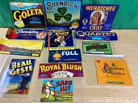Photo of all vintage crate advertising labels laid out showing brand names, colorful vintage designs with fruits, characters and logos.