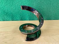 Image showing a single metal taper candle holder with curved spiral design and stud details on the base, on wood surface with green background.