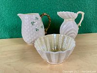 Front view of two porcelain pitchers and one bowl on wooden surface showing texture and design details