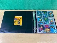 Three-ring binder open showing 9 vintage Marvel holographic character trading cards in protective sleeves and an unopened 1995-96 NBA basketball card pack on inside cover.