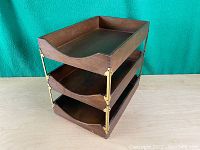 Three quarter angle view of the entire vintage wood desk organizer showing all three trays stacked with brass corner supports.