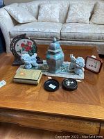 Photo of Asian themed items arranged on a wooden table in front of a sofa showing foo dog figurines, decorative jar, coasters, framed cloth piece, and embroidered cloth.