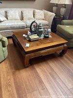 Square wooden coffee table positioned in living room area between sofas and chairs on wood floor, showing table top and side details.