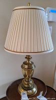 Full view of brass table lamp with pleated cream shade, showing shape and color details.