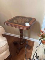 Side angle view showing full profile of square side table with floral decorated top and turned wooden pedestal base.