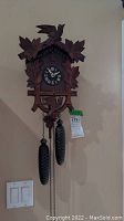 Full front view of German wood cuckoo clock showing carved leaves, birds, and pine cone weights.