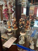 Front view of the five Goebel figurines displayed on glass shelves.