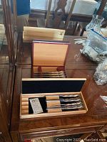 Photo showing three wooden cases containing butter knives and cutlery, including the Henckles and Wusthof cases