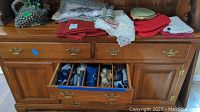Wooden sideboard with assorted kitchen linens on top and an open drawer containing Holmes & Edwards flatware organized in wooden compartments.