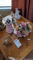 Overview of the lot on a wooden surface showing all figurines, music box, floral arrangement, and candle holder.
