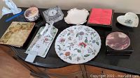 Top-down photo of assorted decorative plates, dishes, clock, and trivets arranged on a dark surface