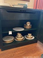 Photo of Lenox Tuxedo dinnerware stacked and arranged on black shelving. Shows various plates and cups stacked neatly.