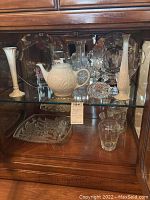 Glass cabinet shelf with Lenox vase, teapot, glass decanter, clear glass bowl, and serving platter.