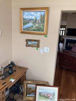 Wall display showing the grouping of framed original art pieces including the largest floral riverside scene and smaller coastal scene.