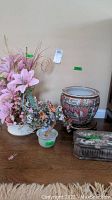 Lot displayed on wooden floor including Lenox ceramic planter with faux floral, jade tree in glass container, nature-themed stone jewelry box and Asian style ceramic planter on wooden stand.