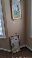 Both artworks shown in corner, framed and hanging on wall or leaned on floor