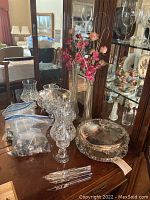 Wide shot showing all items including the crystal vase with flowers, bags of knives, silver plated bowl and tray.