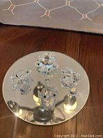 Photo of four small Swarovski crystal animal figurines (frog, turtle, duck, bird) arranged on a reflective round surface.
