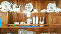 Photo showing multiple tea cups, plates, and a teapot with floral patterns displayed on wooden shelves.